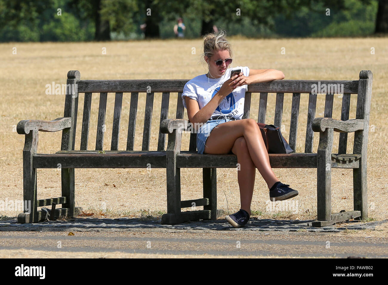 Hyde Park. London. UK 25 July 2018 - A woman sitting on a park bench in  Hyde Park on a very hot and humid day in the capital. According to the Met