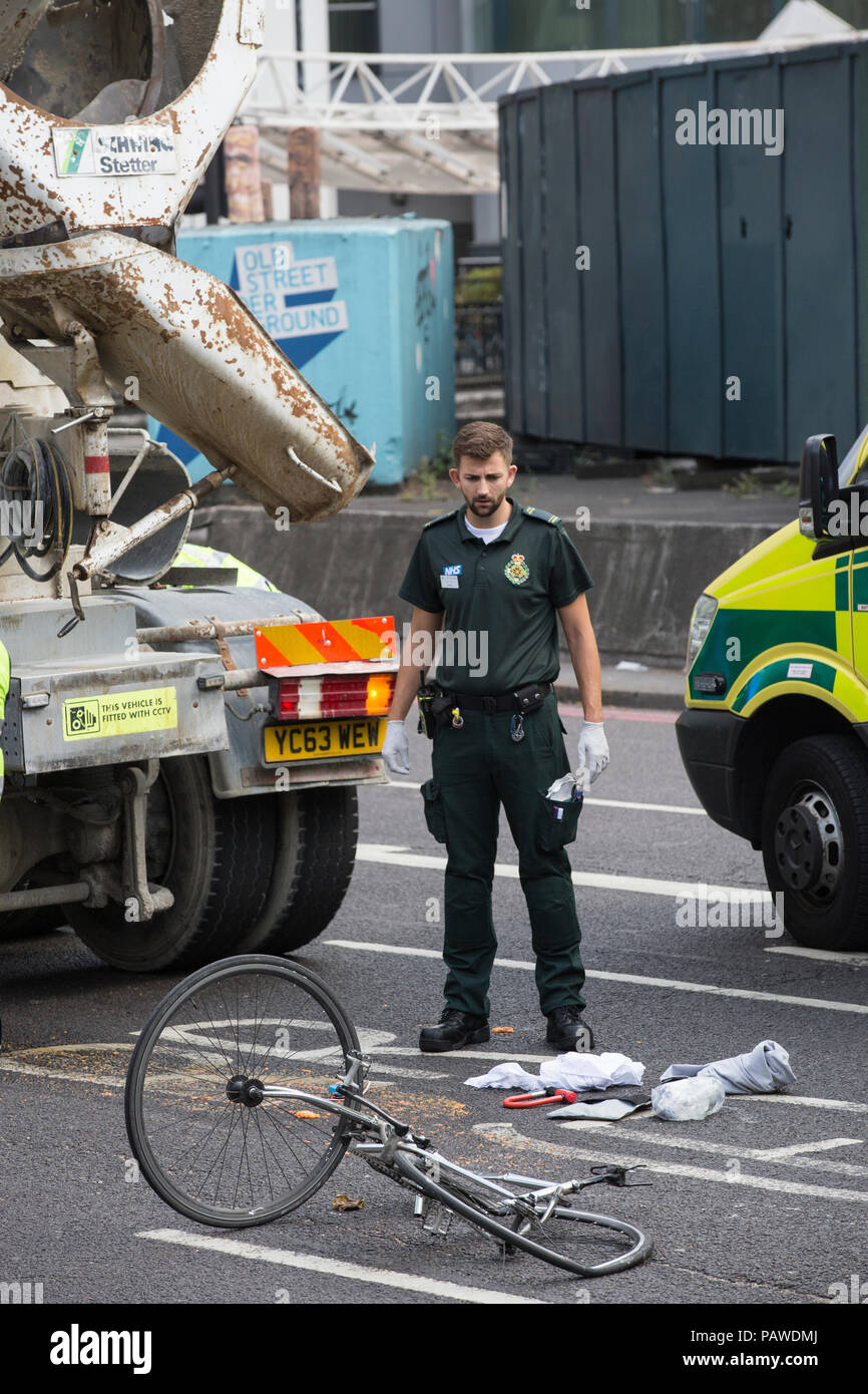 London, UK, 25 July 2018. Old Street Bike accident . 25.07.2018 A paramedic looks down at the remains of a cyclists damaged bycycle after colliding with a concrete lorry on Old Street roundabout this afternoon. Credit: Clickpics/Alamy Live News Stock Photo