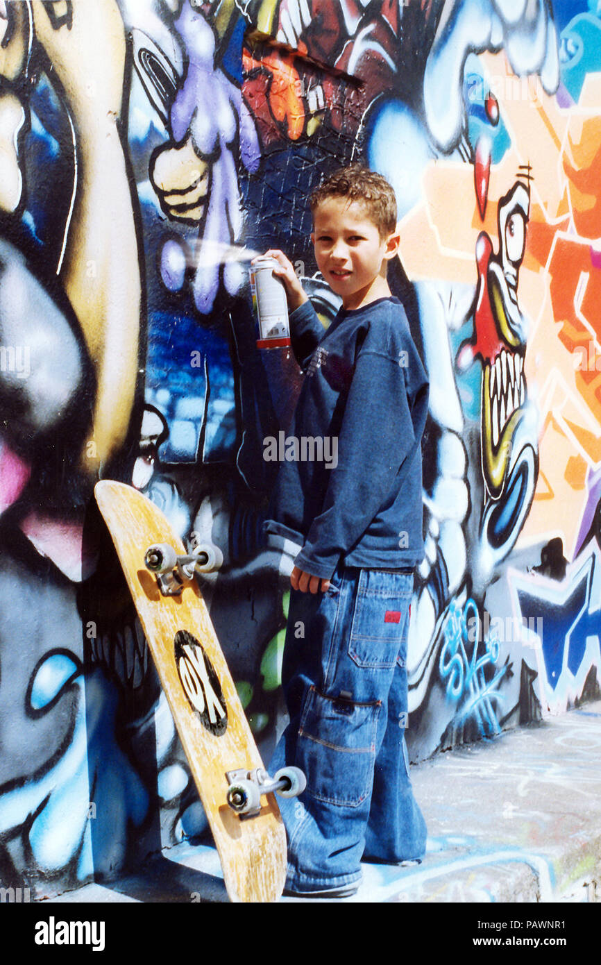 young skateboarder spraying  graffiti on a wall, vandalism Stock Photo