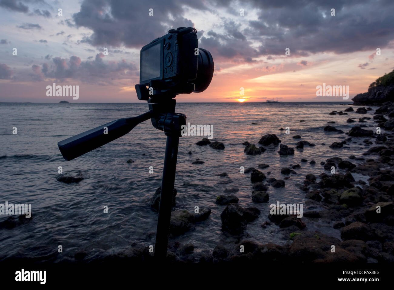 A mirrorless camera and lens on tripod - taking long exposure sunset photos on a beautiful, rocky island beach -Malapascua Cebu - Philippines Stock Photo