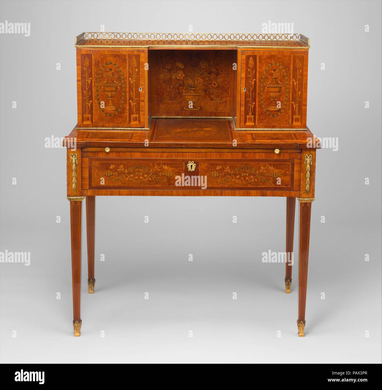 Desk (bonheur du jour). Culture: British. Dimensions: 41 5/16 × 34 7/8 × 18 5/8 in. (104.9 × 88.6 × 47.3 cm). Date: ca. 1780-90.  The idea for this type, with a raised partition in the back, was conceived in Franec about 1750. Extensively used by lady letterwriters, it received the coquettish name bonheur-du-jour. The plain, elegant lines of this example are set off by exceptionally fine, characteristically English marquetry. Museum: Metropolitan Museum of Art, New York, USA. Stock Photo