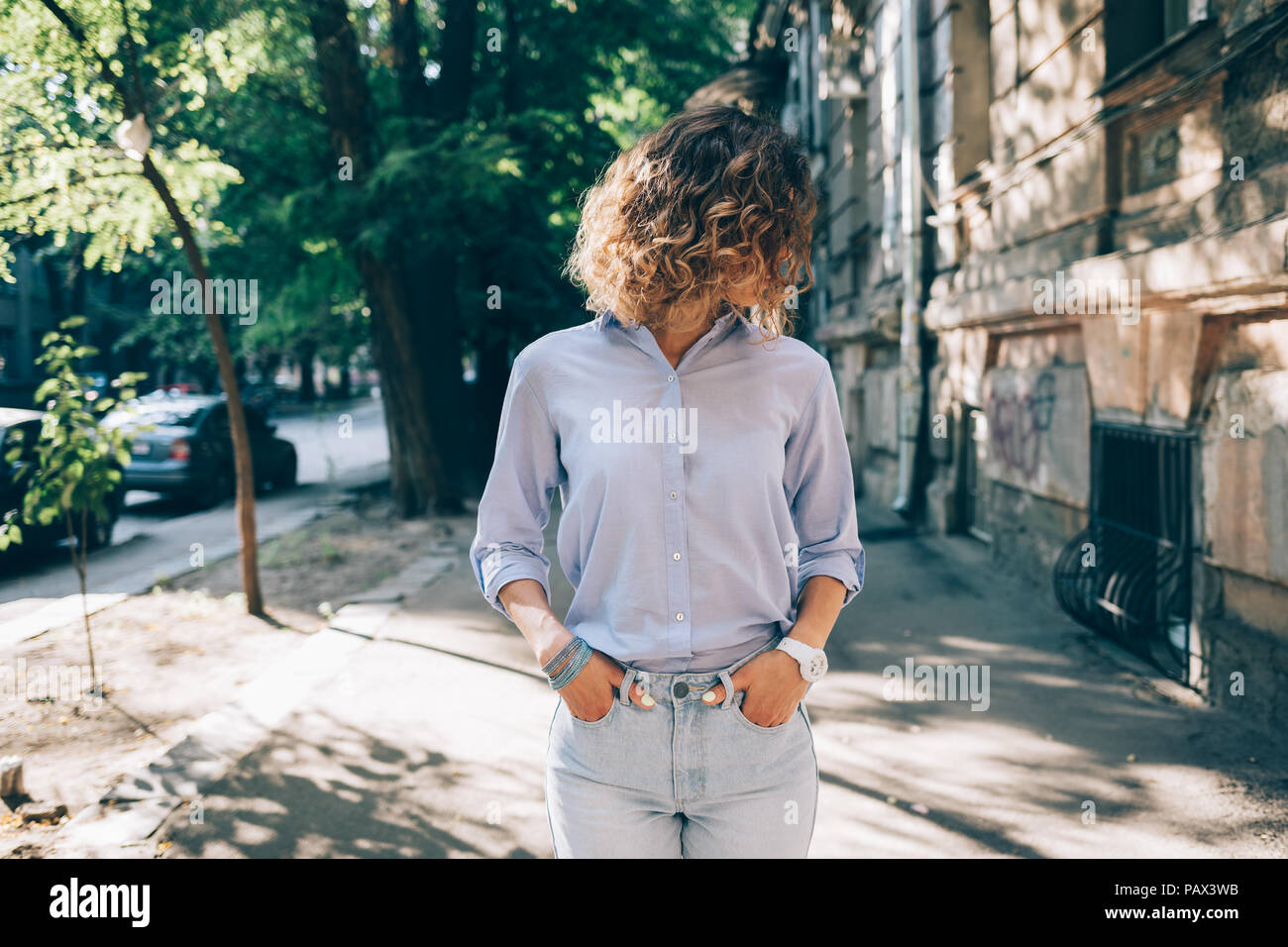 Candid lifestyle photo of fashionable female wearing blue shirt and jeans  posing in old city at sunny summer day. Young woman with fluttering brown  cu Stock Photo - Alamy