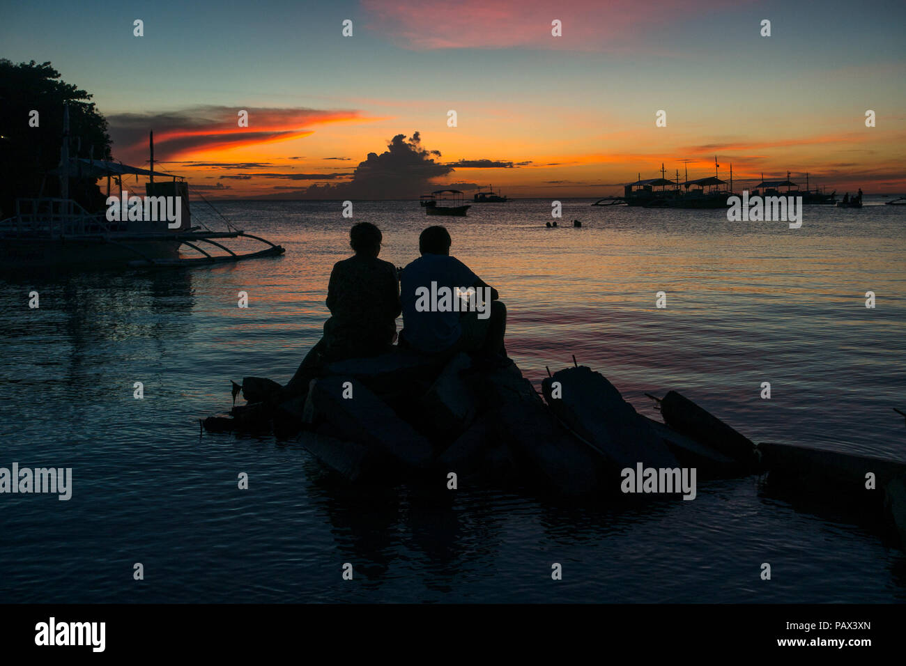 Traveler Couple Sitting on Rocks - Watching an Island Sunset in Cebu, Philippines Stock Photo