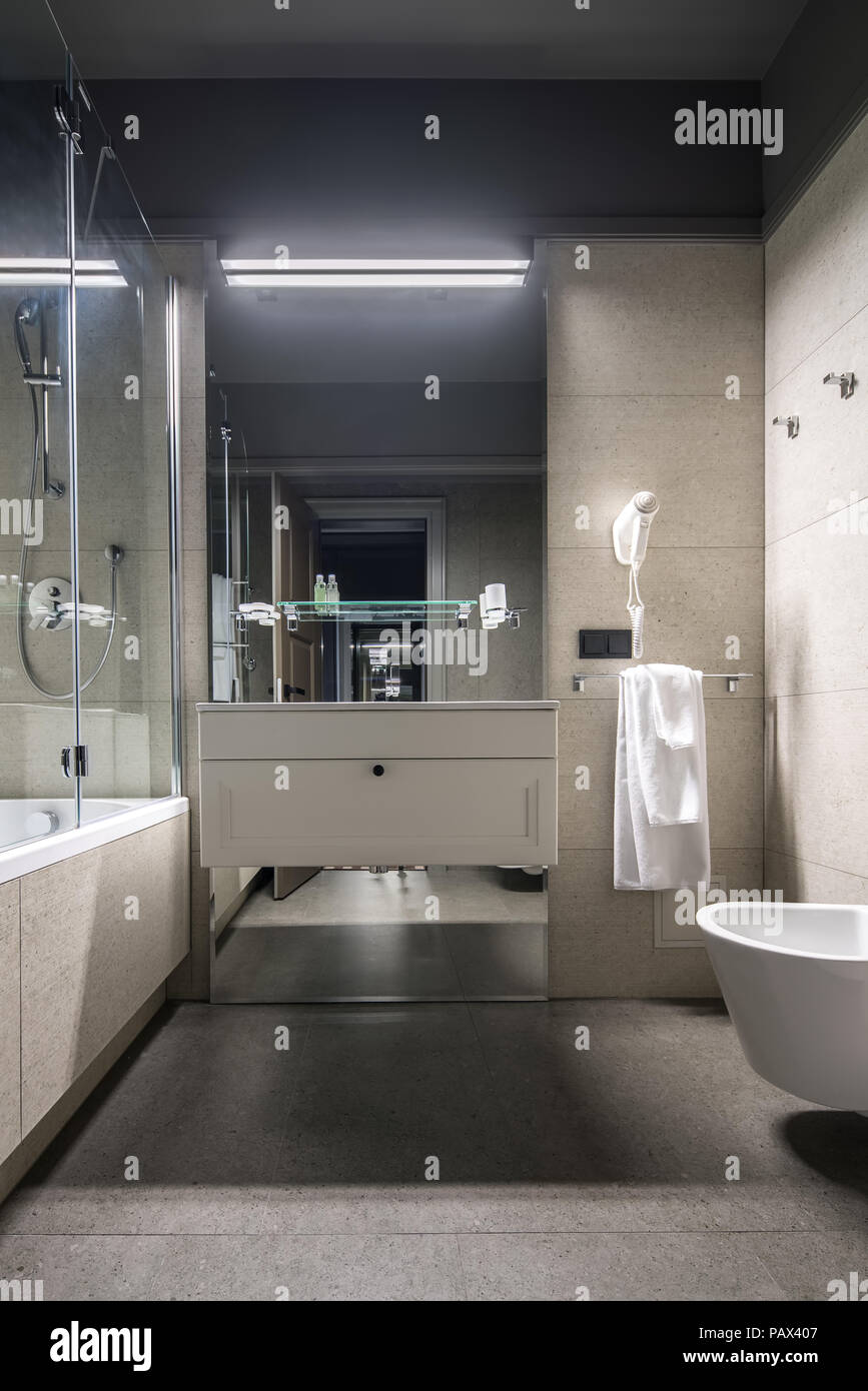 Bathroom In A Hotel With Light Tiled Walls There Is A Bath With A Shower And Glass Partition