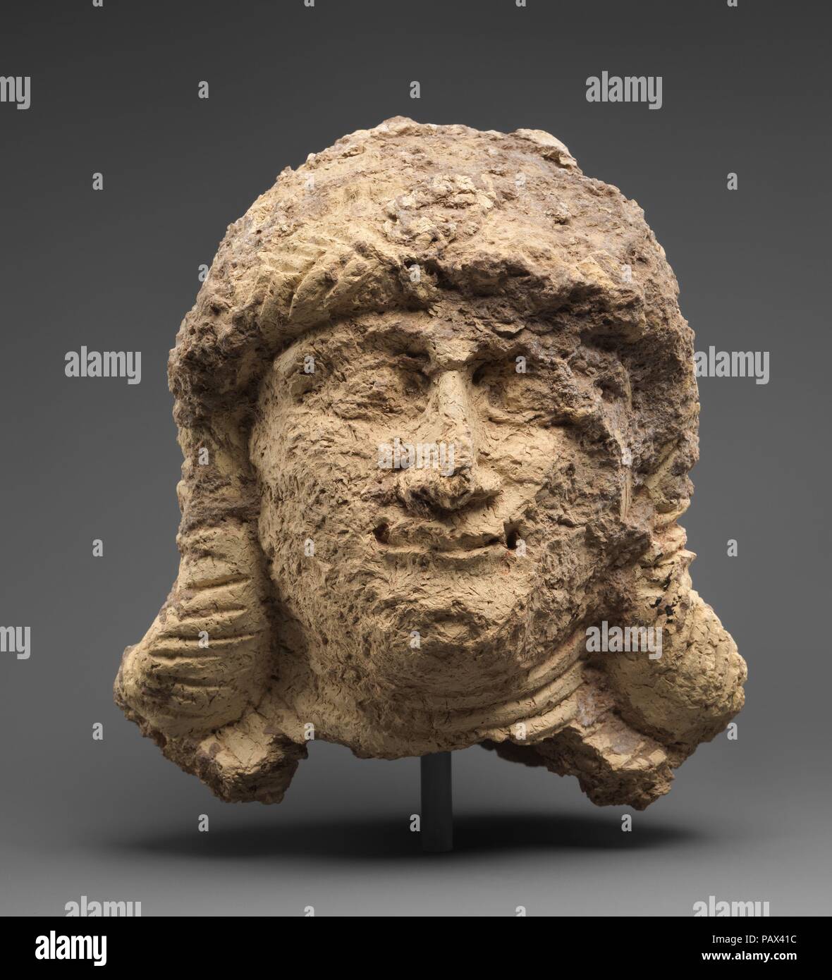 Head of a female. Culture: Babylonian. Dimensions: 7 1/8 x 5 in. (18 x 12.7 cm). Date: ca. 2000-1600 B.C..  This head, broken at the neck and hollow on the inside, depicts a female figure with shoulder length hair arranged in bands of braids around her head and alongside her face. She has large eyes, a small thin smile, and large ears protrude from her hair. Seven bands around her neck represent a multi-strand necklace. The head appears to have been hand-formed out of wads of clay, then fired and painted. The quality of the clay - tempered with organic matter - may account, in part, for its po Stock Photo