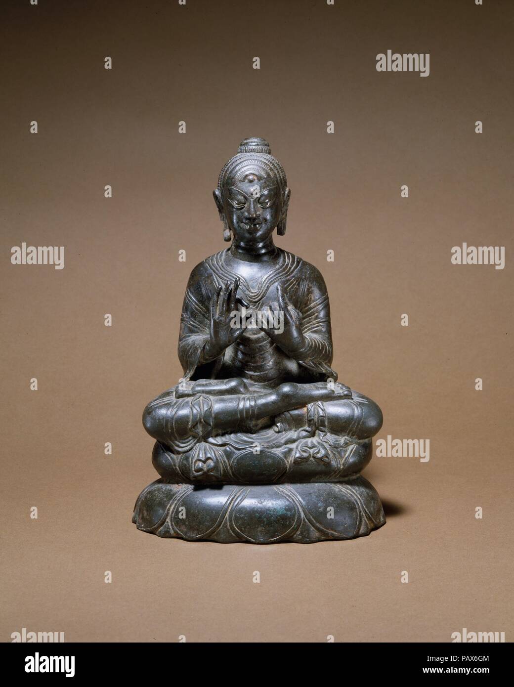 Preaching Buddha. Culture: India (Jammu & Kashmir, ancient kingdom of Kashmir) or Pakistan. Dimensions: H. 8 3/8 in. (21.3 cm). Date: 8th century.  This Buddha, with his legs folded in a full yogic posture and his hands gesturing preaching, invokes the first sermon at Sarnath. The complex treatment of the monastic robes, most notably their pleated ends, is evidence of an unidentified monastic workshop, probably located in Kashmir or the Swat Valley. The treatment of the hair curls is unconventional, as is the extreme stylization of the eyes and eyebrow. Silver inlay marks the eyes and auspicio Stock Photo