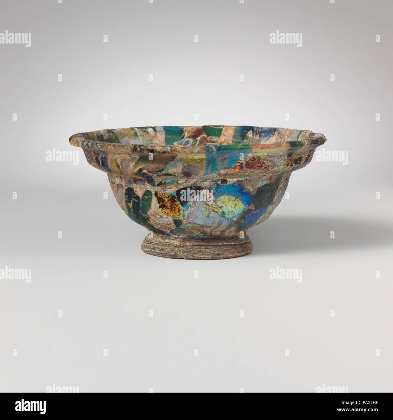 Glass mosaic bowl. Culture: Roman, probably Italian. Dimensions: H.: 1 5/8 in. (4.1 cm)  Diam.: 3 9/16 in. (9 cm). Date: late 1st century B.C.-early 1st century A.D..  Colorless, translucent purple, cobalt blue, turquoise blue, green, honey yellow, and semi-opaque white on body; color(s) of base ring uncertain.  Horizontal everted rim with rounded edge; carinated side, with two convex curves, the upper being narrower and slightly angular, the lower being deeper and more rounded; convex bottom within applied outsplayed base ring with rounded edge.  Composite mosaic pattern formed from polygonal Stock Photo