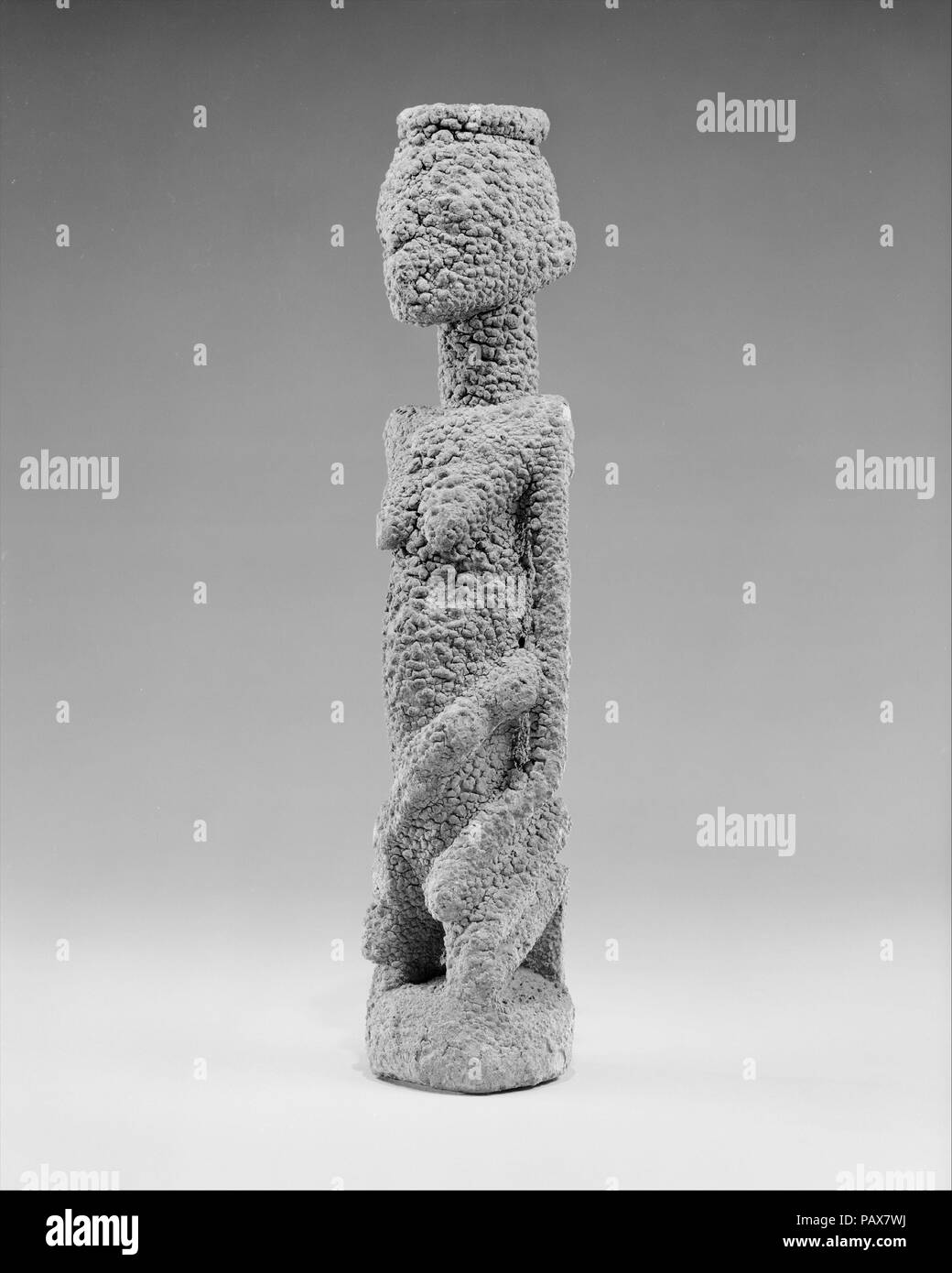 Kneeling Female Figure with Three Children. Culture: Dogon or Tellem  peoples (?). Dimensions: H. 13 x W. 3 x D. 2 5/8 in. (33 x 7.6 x 6.7 cm). Date: 15th- 19th century (?).  The subject of this intimately-sized sculpture is a kneeling female figure. The woman is shown sitting on her knees with flexed feet and hands resting on her thighs. The posture's grounded and meditative quality is accentuated by the compact rendition of the lower body whose center of gravity is concentrated around the circular base. In contrast to the slim lower limbs, the sculptor elongated and enlarged the figure's tor Stock Photo