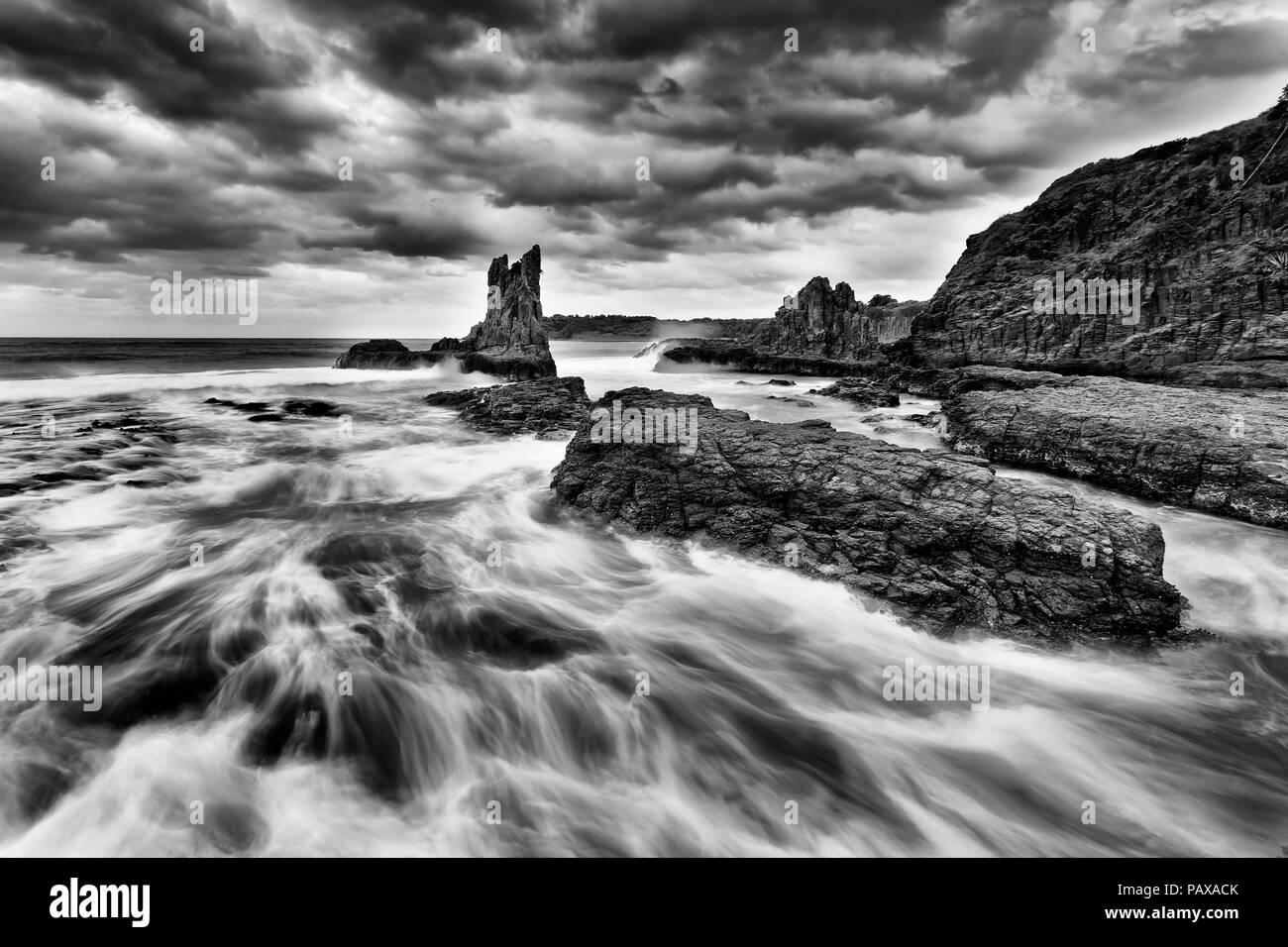 Eroded golden sandstone cathedral rocks at Bombo beach in Kiama, NSW, Australia, at stormy sunset under cloudy sky in black white. Stock Photo