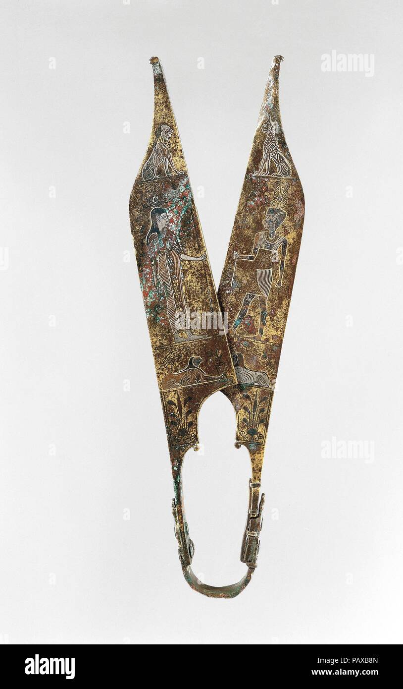 Shears. Dimensions: Height: 9 5/16 in. (23.7 cm). Date: A.D. 2nd century perhaps.  This piece is remarkable for its rich inlays. Both sides of each blade are decorated with three registers of figures. Whoever created the design clearly had a sense of humor; when the shears are closed, the top register brings a dog face-to-face with a cat on one side and a lion on the other.   The combination of vague iconography, attenuated drawing, and dour expressions marks the shears as in an 'Egyptianizing' rather than an actual Egyptian style. Perhaps they served a ritual function at an Isis sanctuary at  Stock Photo