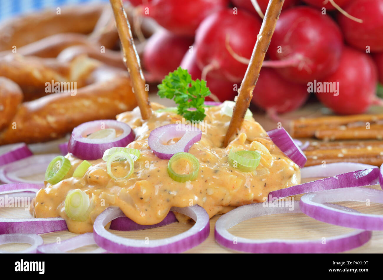 Bavarian cheese specialty called 'obazda', served with onion rings, pretzels and radishes on a wooden plate Stock Photo