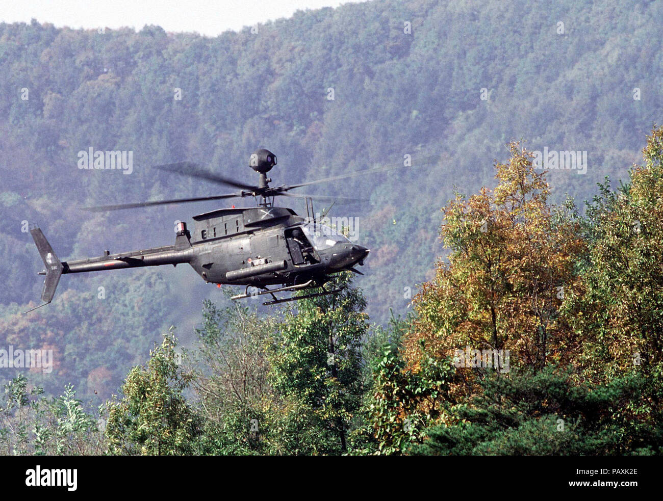 A US Army OH-58D helicopter with the 4th Squadron, 7th Cavalry Regiment hovers over the tree tops as it prepares to support armor belonging to C Troop of the 4-7 Cavalry during maneuvers and gunnery training at t(. A US Army OH-58D helicopter with the 4th Squadron, 7th Cavalry Regiment hovers over the tree tops as it prepares to support armor belonging to C Troop of the 4-7 Cavalry during maneuvers and gunnery training at the Korea Training Center, Republic of Korea on Oct. 25, 1998.  The center is manned throughout the year and various armored units rotate through training scenarios to meet y Stock Photo