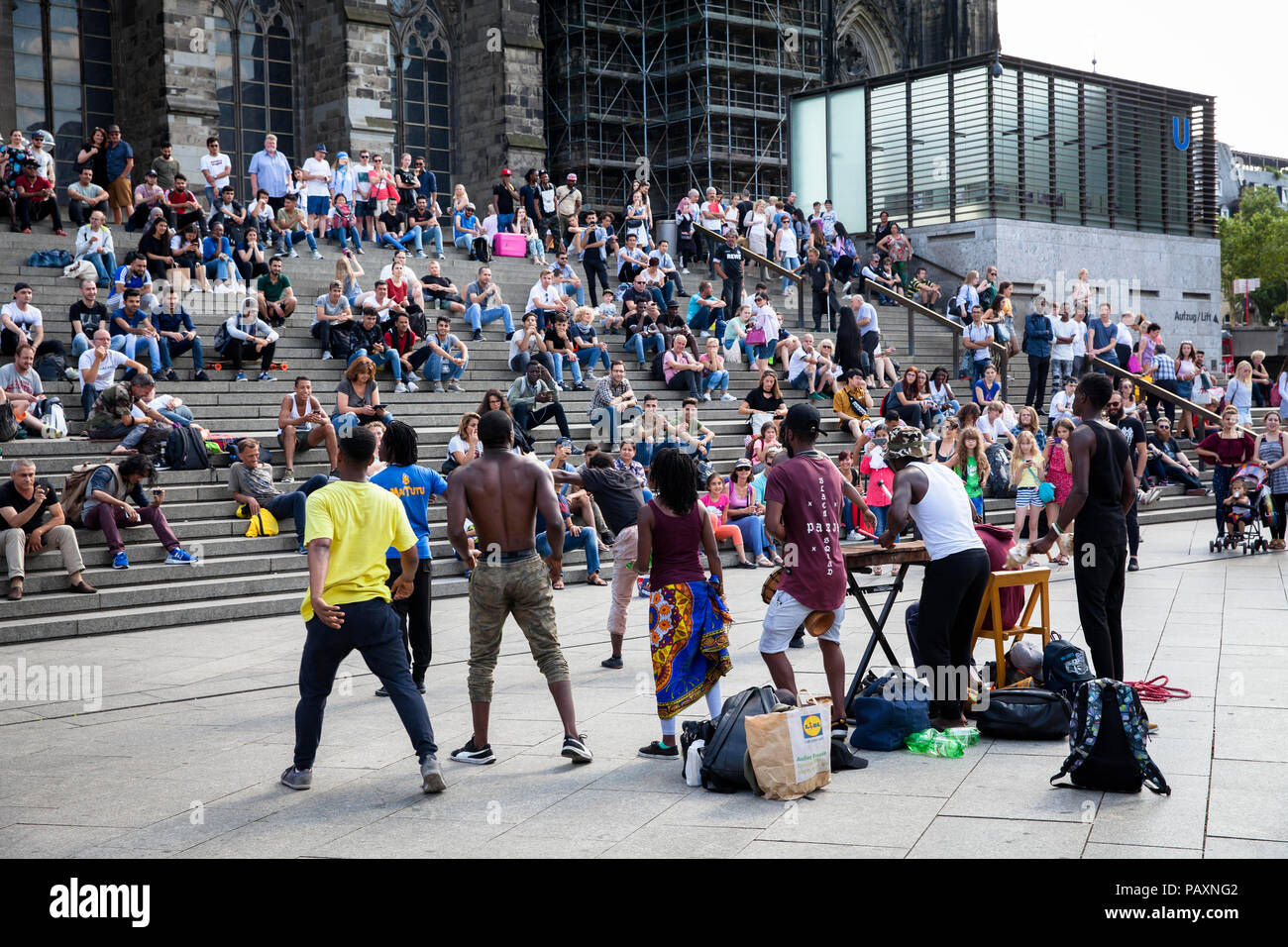 people sitting on the stairs form the cathedral square to the main station and listen street musicians, Cologne, Germany.  Menschen sitzen auf der Tre Stock Photo