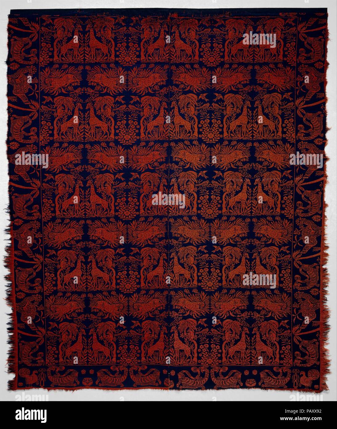 Coverlet. Culture: American. Dimensions: 85 x 73 in. (215.9 x 185.4 cm). Date: ca. 1840-50.  This coverlet is woven with red and blue wool warps and red and blue wool wefts in two panels and seamed at the center. The field shows a menagerie of animals, including giraffes, leopards, monkeys, and birds. The borders have images of an alligator eating a snake alternating with a pouncing leopard. In contrast to the predominant jungle motifs, domesticated fowl are depicted on the corner blocks. Museum: Metropolitan Museum of Art, New York, USA. Stock Photo