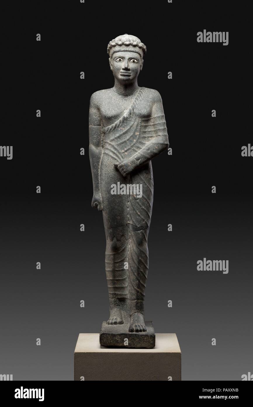 Official with Pleated Costume. Dimensions: H. 116.5 cm (45 7/8 in.). Date: 150-1 BC.  Striding draped figures appear in the Egyptian statuary repertoire in the mid-second century B.C.; such statues seem often to have stood in front of temples pylons. Possibly the diadem worn by this figure indicates a priestly office.  Although only now appearing in statuary, the figure's distinctive garments seem to have actually been worn in Egypt already for some centuries. The ensemble has three elements: a sleeved tunic is worn closest to the body; over that is wrapped a long fringed skirt whose edge is v Stock Photo