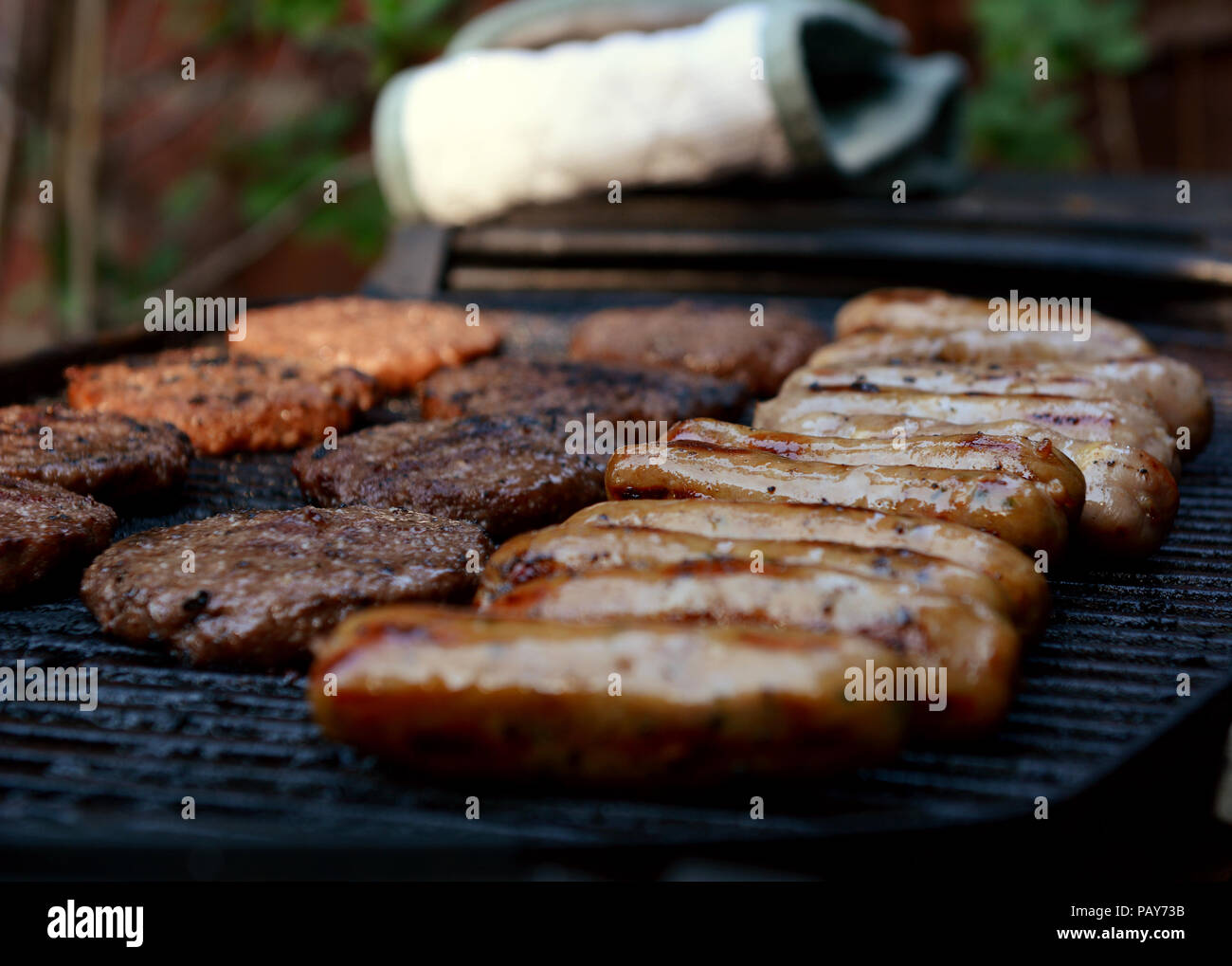 Rows of cooked sausages and hamburgers on an open barbecue grill Stock Photo