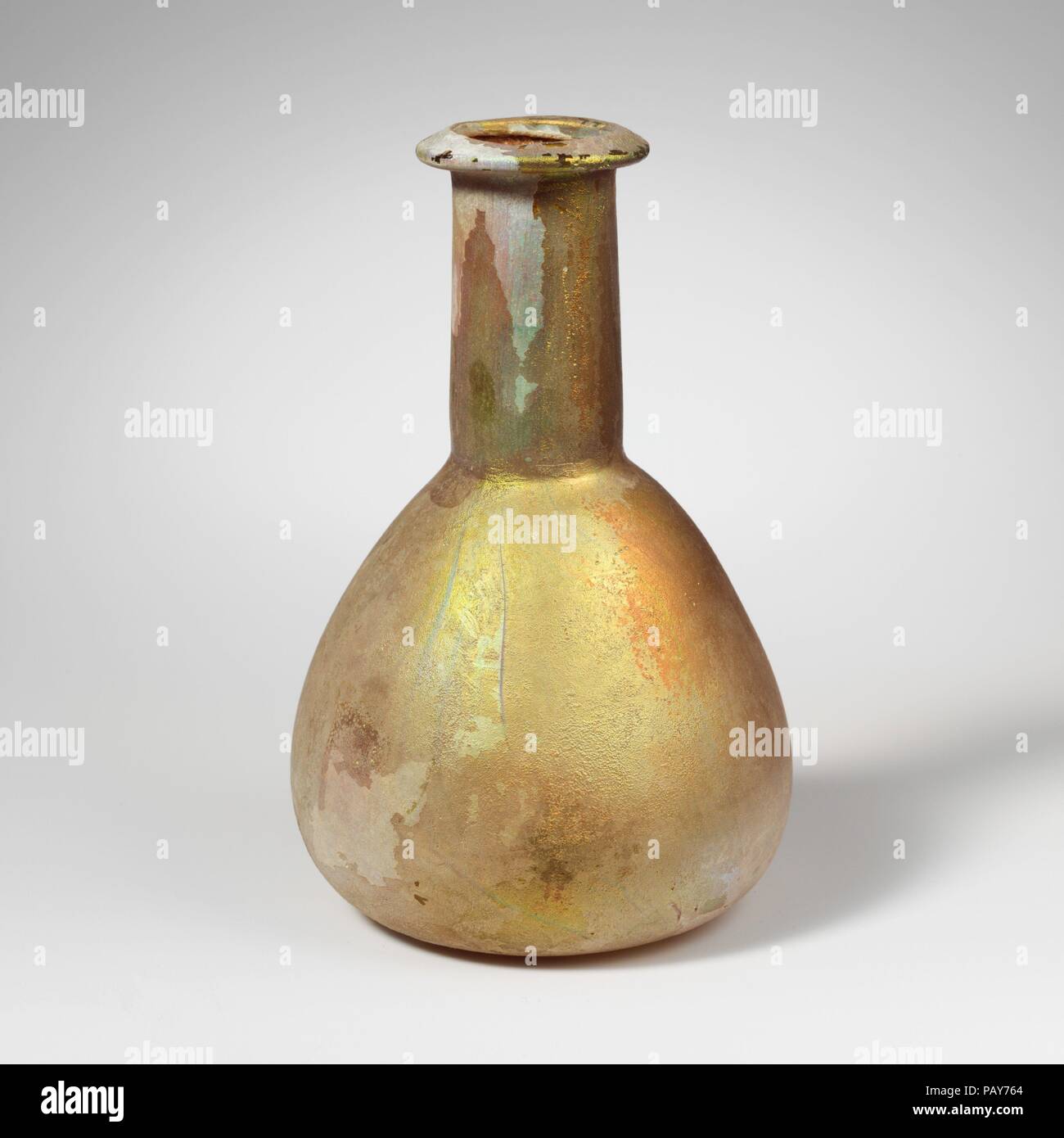 Glass perfume bottle. Culture: Roman. Dimensions: 5 3/16 in. (13.1 cm)  Other: 3 5/16 in. (8.4 cm)  Diam. of rim: 1 1/2 in. (3.8 cm). Date: 1st-2nd century A.D..  Translucent pale blue green.  Rim folded out, over, and in, with beveled upper surface and rounded lip around mouth; cylindrical neck, expanding downward and slightly tooled in around base; broad, piriform body; convex bottom, slightly flattened at center. Fairly thick and heavy glass.  Intact; many pinprick bubbles; deeply pitted and weathered, with brilliant iridescence on most of surface. Museum: Metropolitan Museum of Art, New Yo Stock Photo