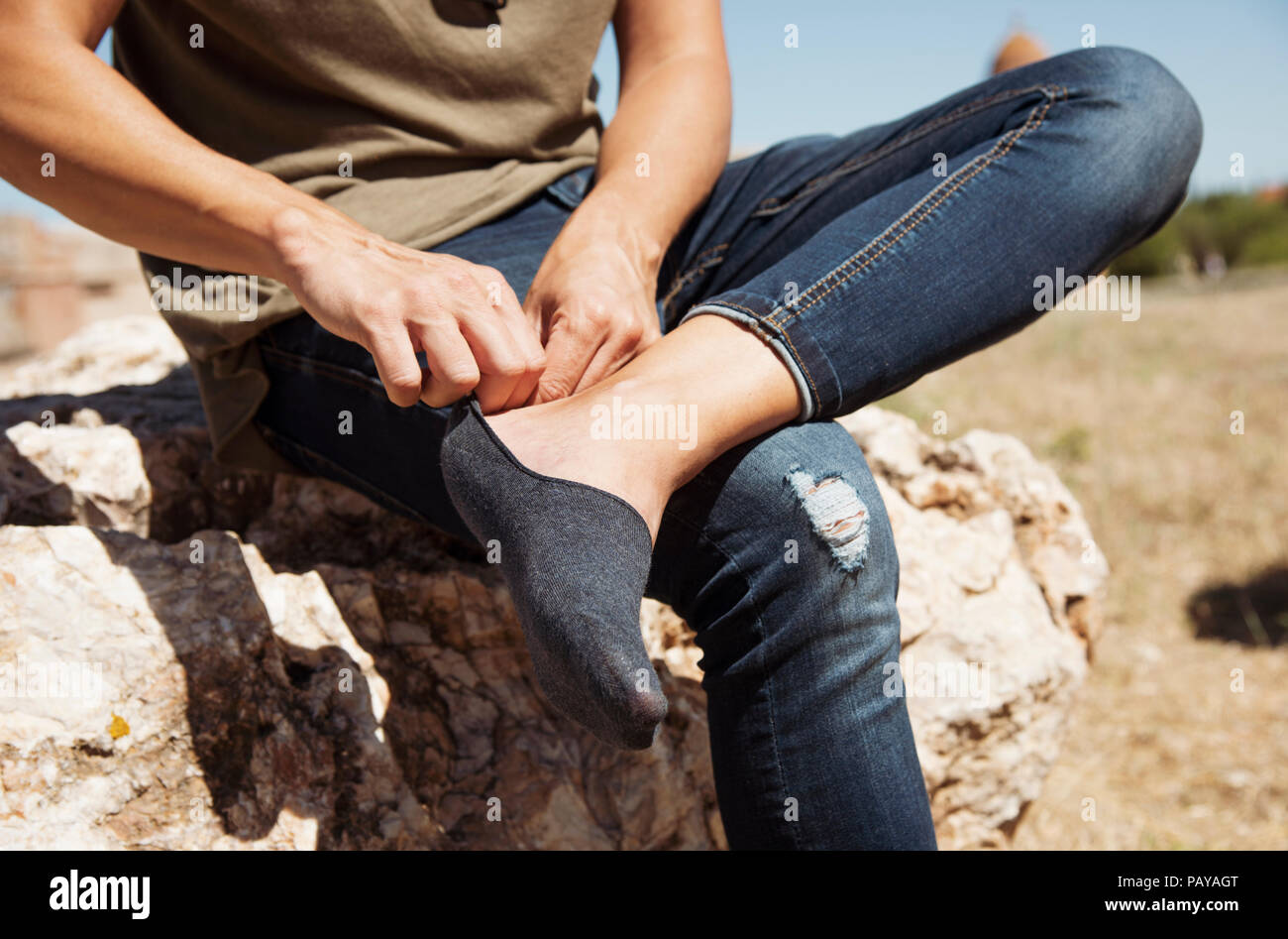 closeup of a young caucasian man sitting on a rock outdoors putting on or taking off a a low cut sock Stock Photo