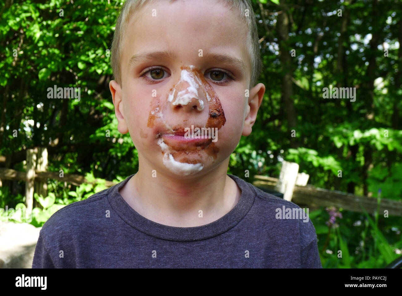 A young boy (6 yr old) with face covered in chocolate after eating an ice cream Stock Photo