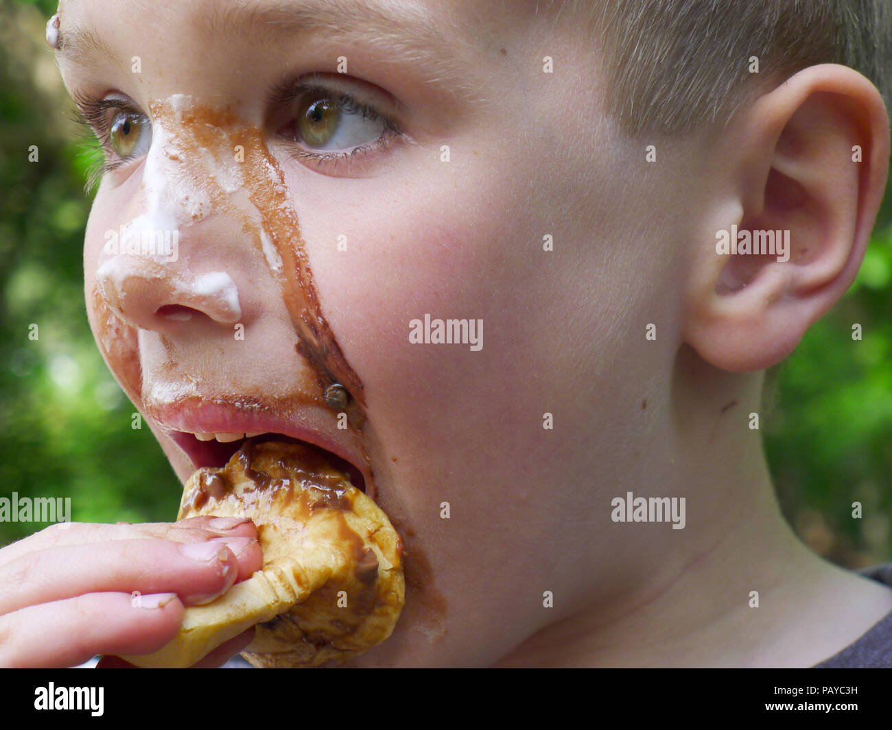 A young boy (6 yr old) with face covered in chocolate after eating an ice cream Stock Photo