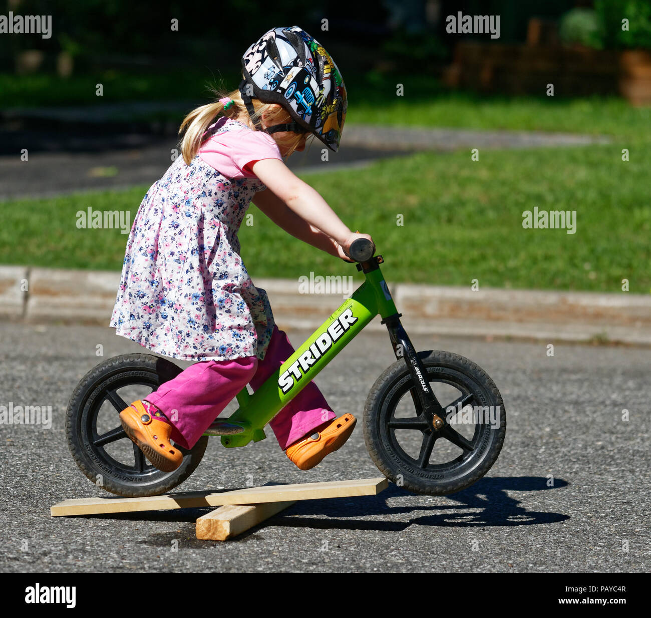 A little girl (3 yr old) riding her balance bike across a jump made of bits of wood Stock Photo