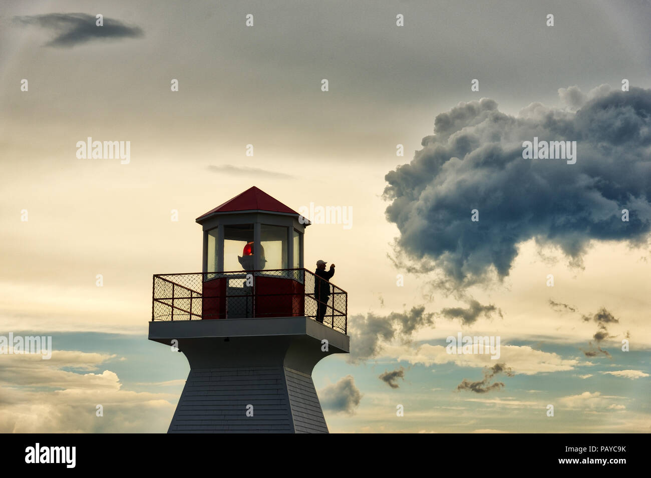 A man stood taking photos on the lighthouse at sunset in Carleton in Gaspesie, Quebec Canada Stock Photo