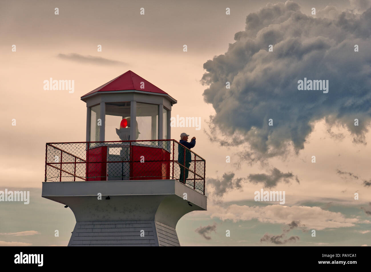 A man stood taking photos on the lighthouse at sunset in Carleton in Gaspesie, Quebec Canada Stock Photo