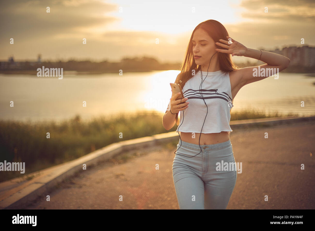 Young beautiful caucasian blonde girl listening to music with smartphone walking in the city with headphones smiling - relax, youth, emancipation concept Stock Photo