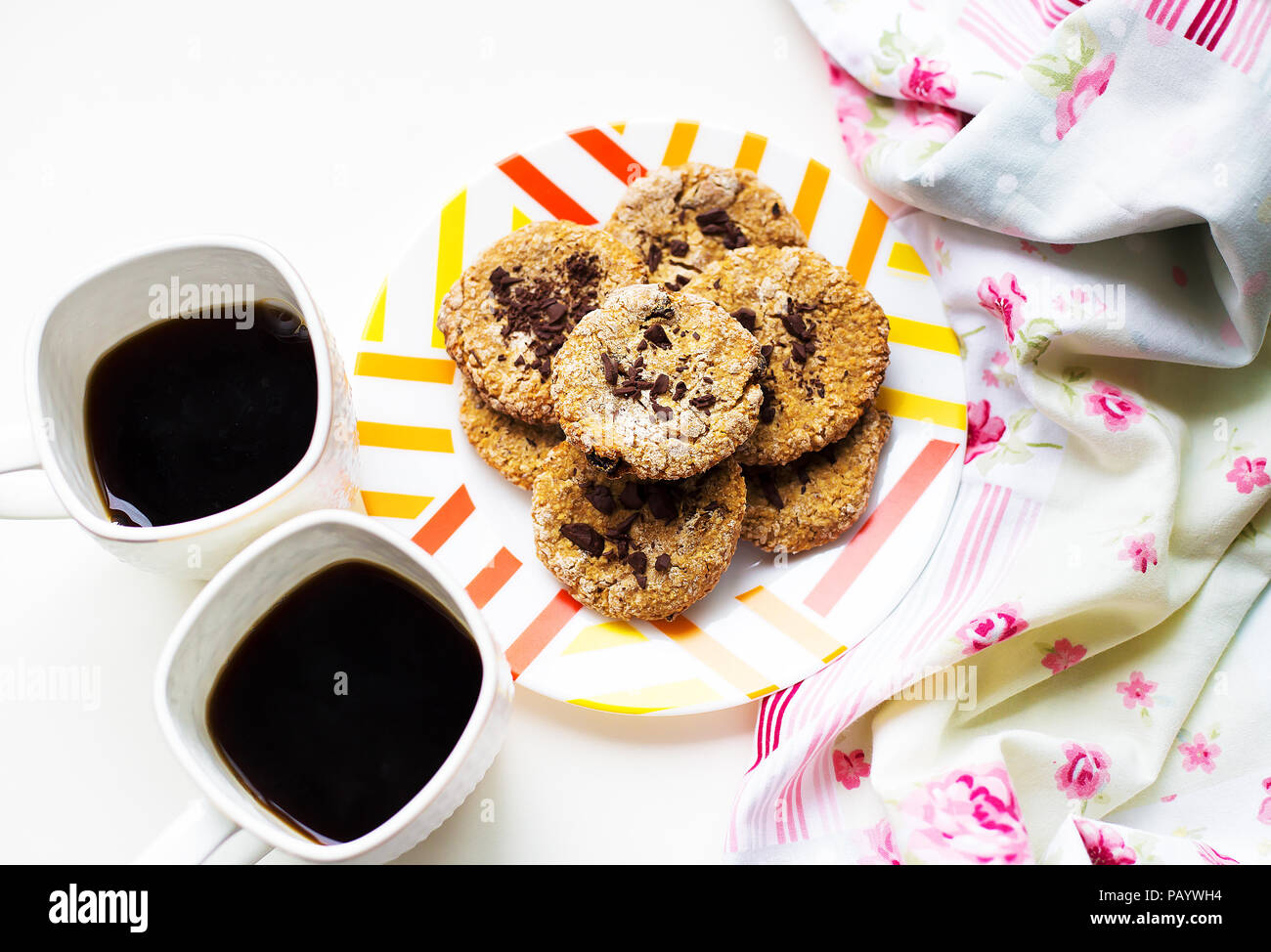 Oatmeal cookies with chocolate on a plate with bright cloth and two cups of coffee Stock Photo