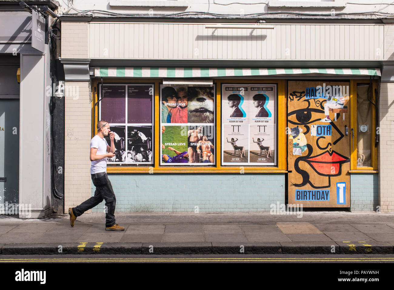 Man walking in Old Compton Street in Soho  in front of a wall covered in billboards and murals Stock Photo