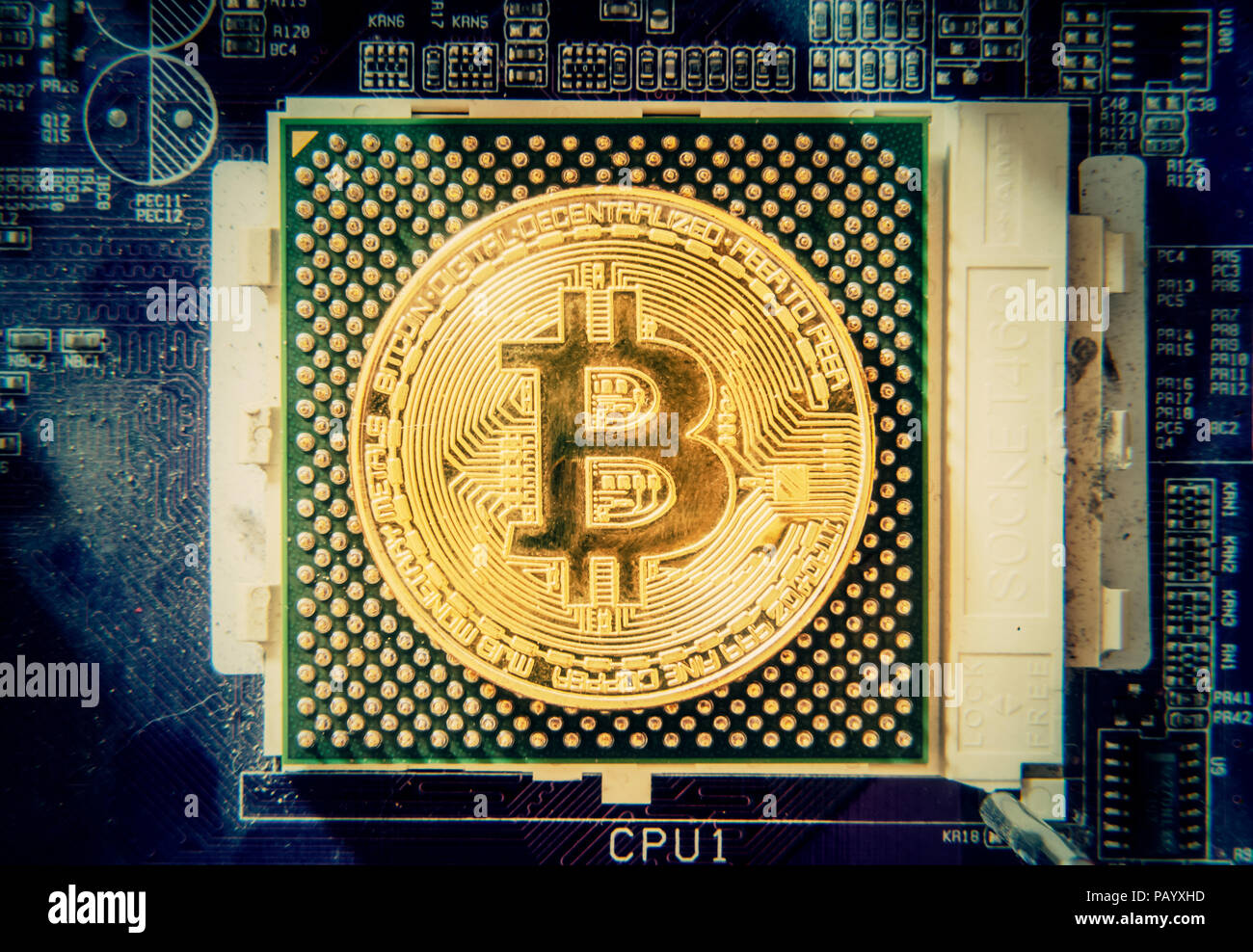 A big golden physical bitcoin (digital virtual crypto-currency) replacing a CPU on a motherboard. Stock Photo