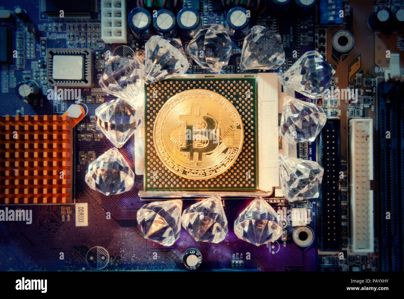 A big golden physical bitcoin (digital virtual crypto-currency) replacing a CPU on a motherboard, surrounded by shiny diamonds. Stock Photo