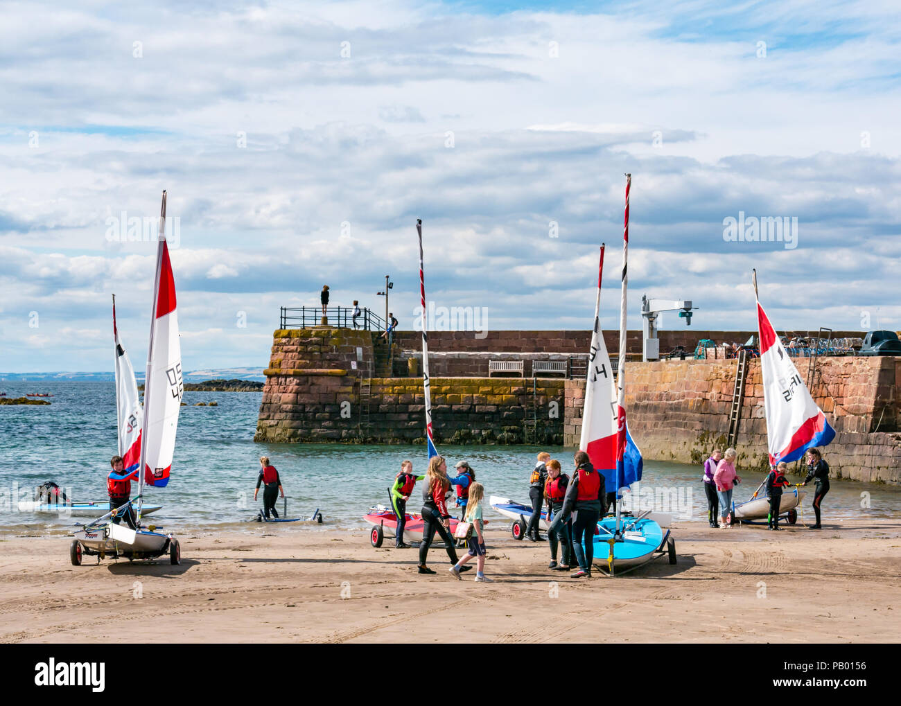 Boat club with people pulling sailing dinghies out of sea onto trailers at West bay beach with harbour wall and entrance, North Berwick, East Lothian, Scotland, UK Stock Photo