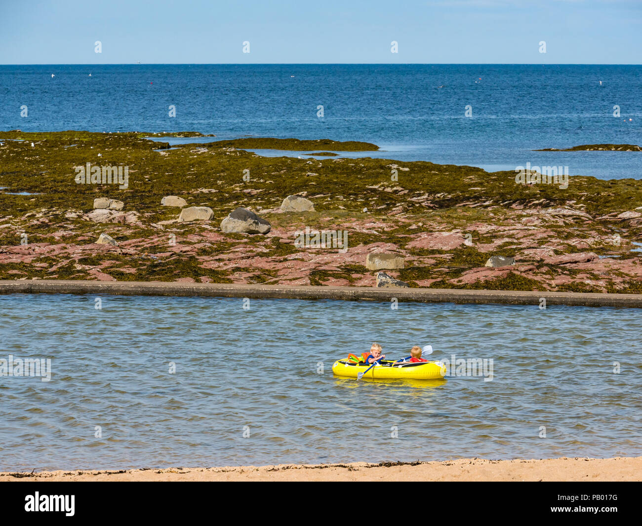 Young children in inflatable rowing boat in outdoor tidal bathing pool with Firth of Forth, Milsey Bay, North Berwick, East Lothian, Scotland, UK Stock Photo