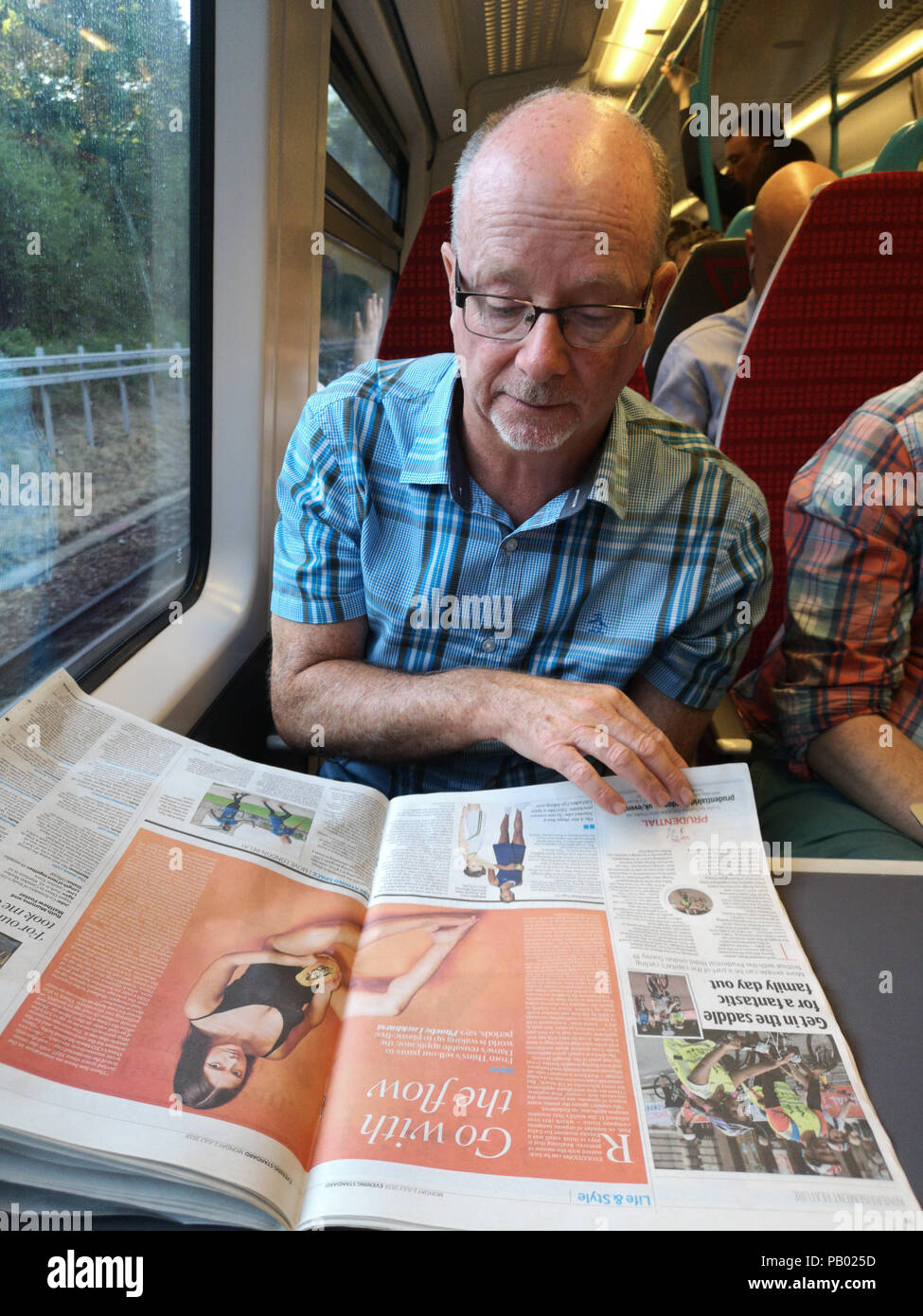 Middle aged commuter reading the Evening Standard whilst travelling on a train from London to Brighton. July 2nd 2018 Picture by James Boardman Stock Photo