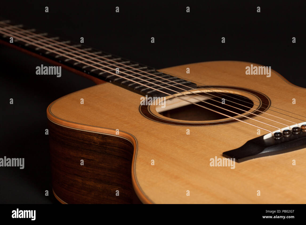 High quality steel-string acoustic guitar. Hand-made wooden musical instrument with European spruce wood top and Ovangkol side. Close-up of body and s Stock Photo