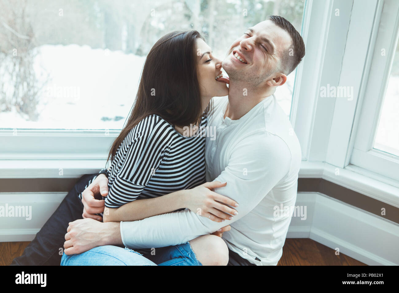 Portrait of beautiful romantic funny young Caucasian couple man woman in  love hugging, kissing, indoors at home sitting by window, toned with  filters Stock Photo - Alamy