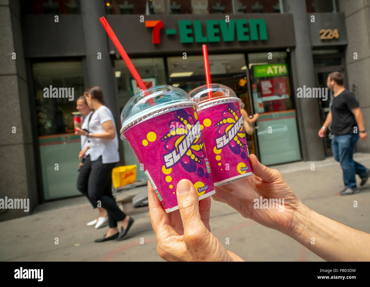 A Slurpee lover displays her Slurpees outside a 7-Eleven store in New York on Wednesday, July 11, 2018 (7-11, get it?), Free Slurpee Day! The popular icy, slushy, syrupy drinks are available in regular and diet flavors, in combinations, and the stores have stocked up with extra barrels of syrup to meet the expected demand. According to the meticulous figures kept by 7-Eleven they sell an average of 14 million Slurpees a month and over 150 million Slurpees a year.  (© Richard B. Levine) Stock Photo