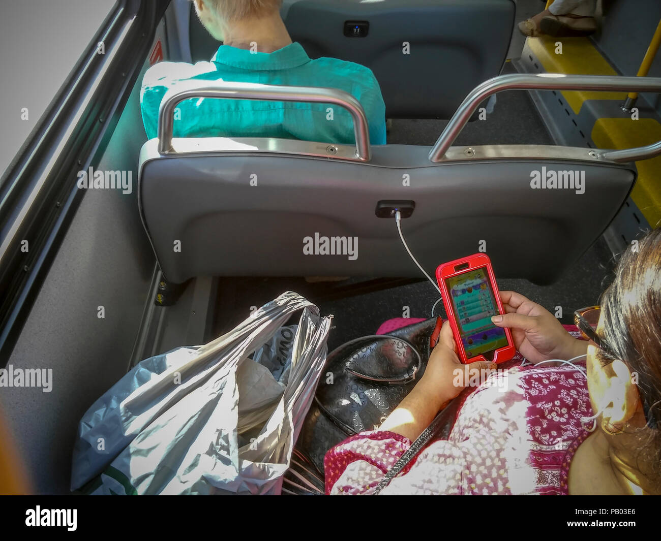 A passenger on a Select Bus Service bus on the M23 route in Chelsea in New York on Saturday, July 14, 2018 plugs her smartphone into a USB port. NYCTA President Andy Byford recently announced the 'Bus Action Plan', a comprehensive overhaul of the city's surface transportation system including the introduction of double-decker buses, increased ability to pay prior to boarding and an app to check whether seats are available. Bus ridership has fallen off in the city.  (Â© Richard B. Levine) Stock Photo