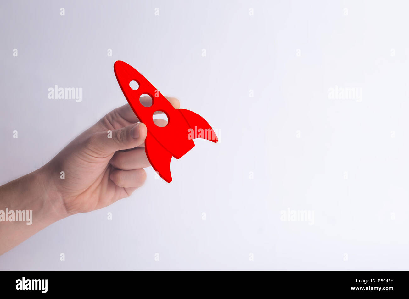 Wooden red rocket in hand on a white background. A man is playing with a rocket. Minimalism, space travel and tourism, commercial rocket launches into Stock Photo