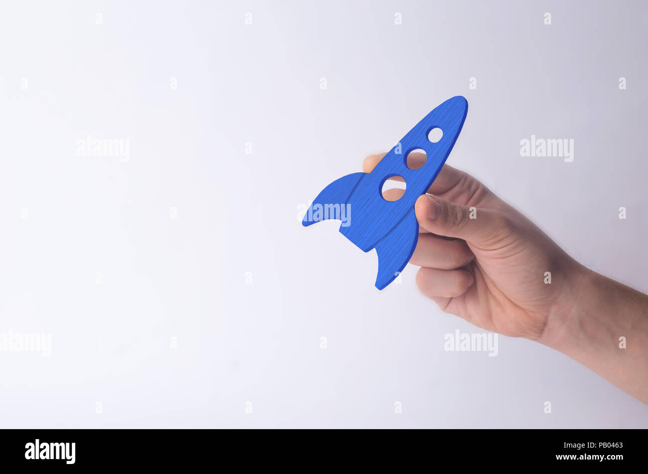 Wooden blue rocket in hand on a white background. A man is playing with a rocket. Minimalism, space travel and tourism, commercial rocket launches int Stock Photo