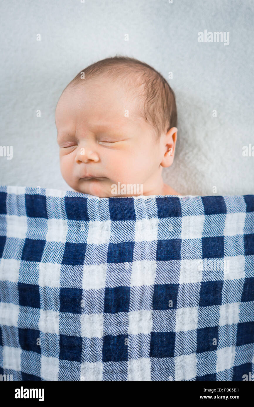 Newborn baby boy sleeping in bed with checkered blue and white blanket