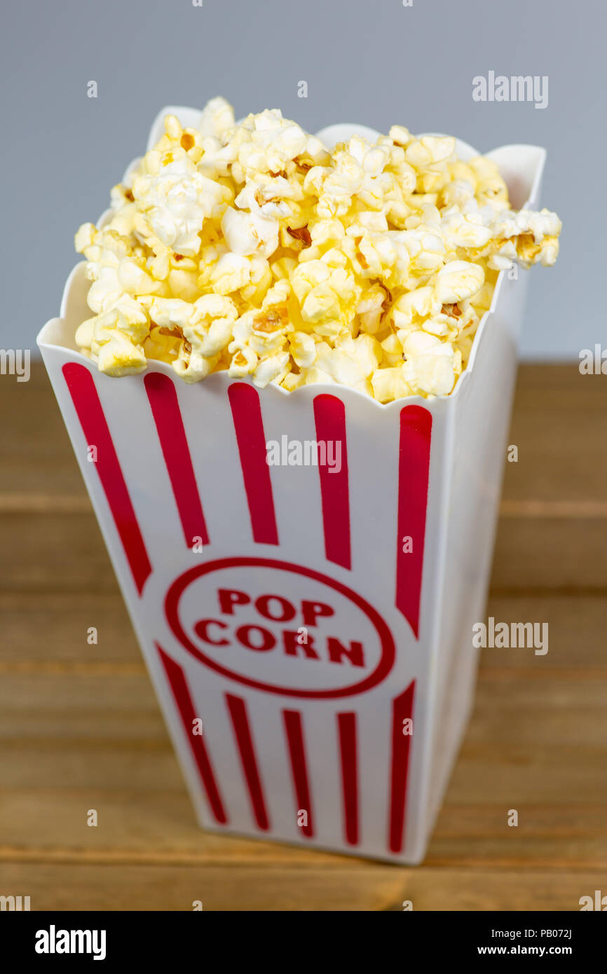 A red stripped popcorn small bucket overflowing with popcorn on a white counter Stock Photo
