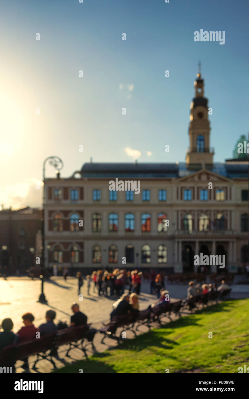 In the spring of people sitting on a bench in front of city hall in the old town of Riga blurry Stock Photo
