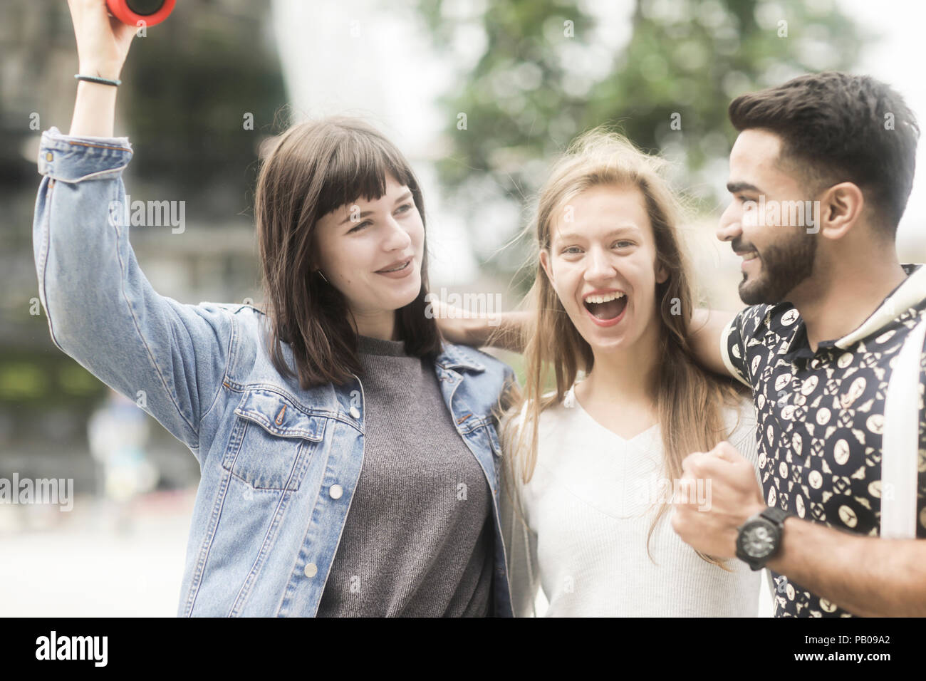 Three friends with their arms around each other listening to music Stock Photo