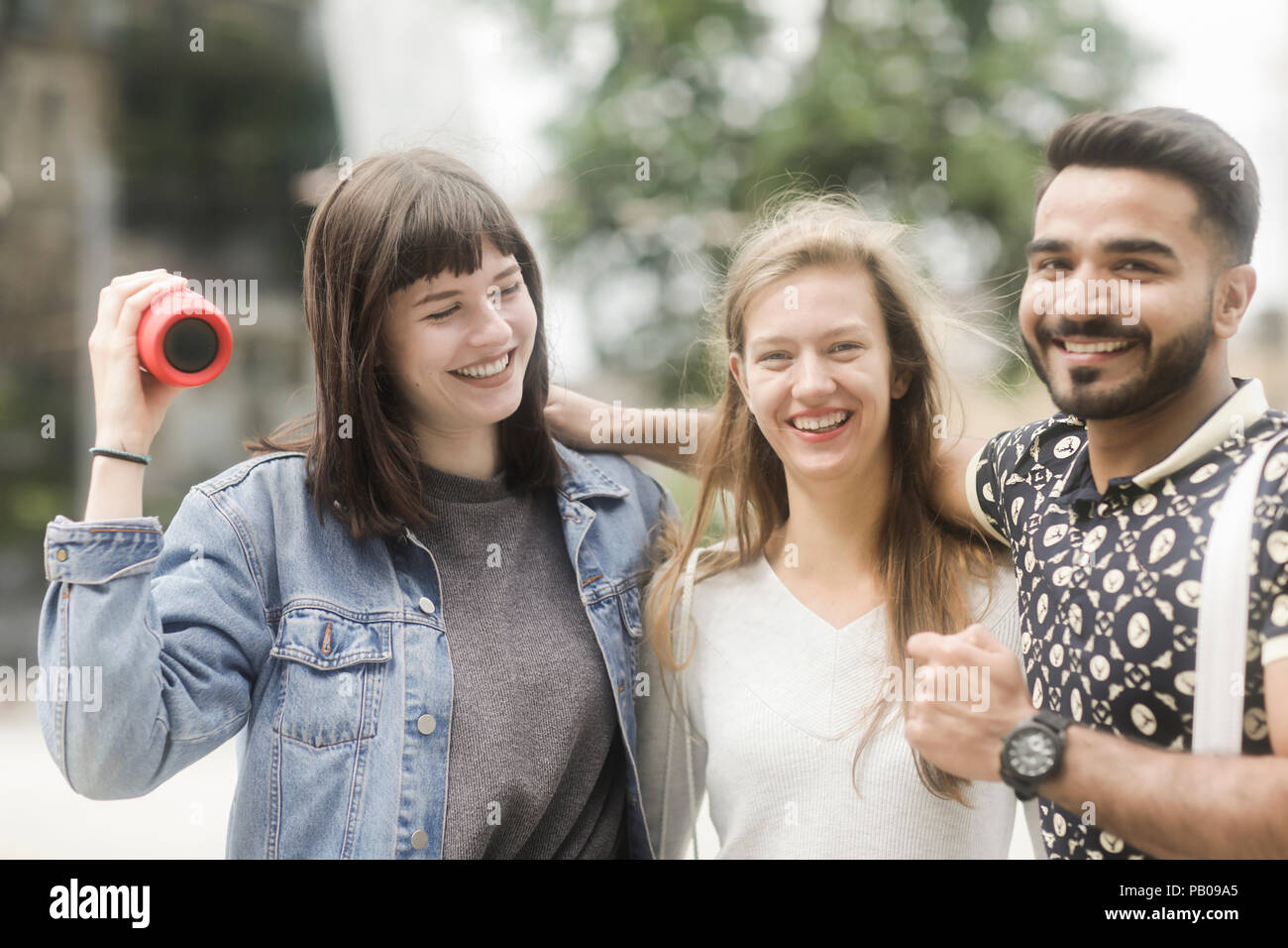 Three friends with their arms around each other listening to music Stock Photo