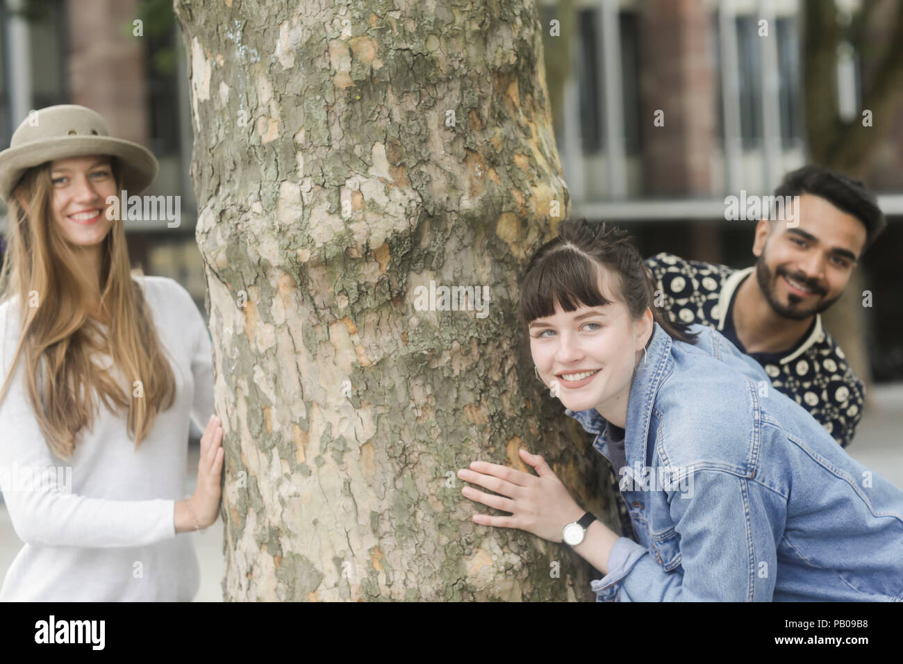 Three friends messing about by a tree in the city Stock Photo - Alamy