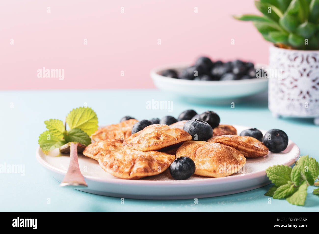 Dutch mini pancakes called poffertjes with blueberries, sprinkled with powdered sugar. Healthy food concept with copy space. Stock Photo