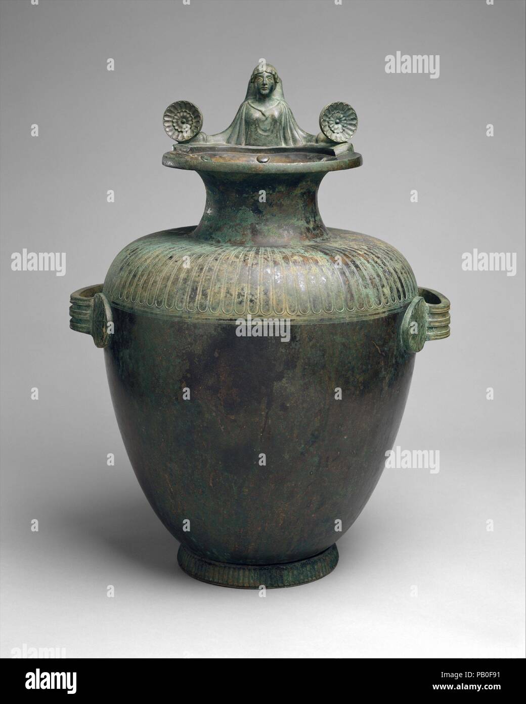 Bronze hydria (water jar). Culture: Greek, Argive. Dimensions: H. with handle 20 1/4 in. (51.41 cm). Date: mid-5th century B.C..  Inscribed on top of the mouth 'one of the prizes from Argive Hera'  This hydria, like Greek art in all its forms, is marked by clearly defined parts organized into a harmonious well-proportioned whole. The plain body swells gently to the shoulder zone, which turns inward with a soft, cushionlike curve. The shoulder is decorated with a simple shallow tongue pattern that echoes the vertical ribbing on the foot. The neck shoots up from the shoulder to a flaring mouth f Stock Photo