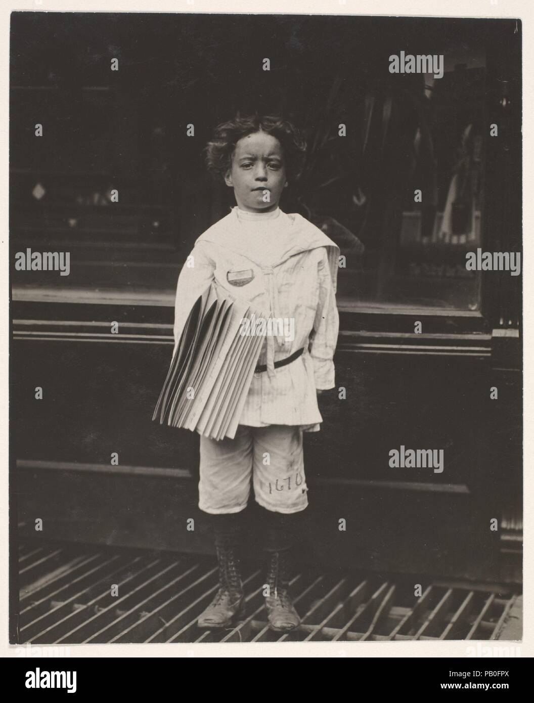 Jo Lehman, a 7 year old newsboy. 824 Third Ave., N.Y. City. He was selling in this Saloon. I asked him about the badge he was wearing.  'Oh! Dat's me bruder's,' he said. Location: New York, New York. Artist: Lewis Hine (American, 1874-1940). Dimensions: Image: 11.6 x 9.5 cm (4 9/16 x 3 3/4 in.). Date: July 1910.  Trained as a sociologist at Columbia University, Hine gave up his teaching job in 1908 to become a full-time photographer for the National Child Labor Committee. The success of the reform agency, created four years earlier, was largely dependent on its ability to sway public opinion.  Stock Photo